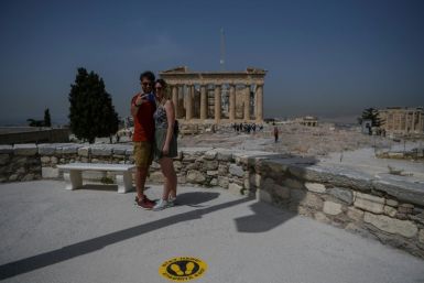 A couple takes a selfie next to a sticker marking social distance in front of the Parthenon