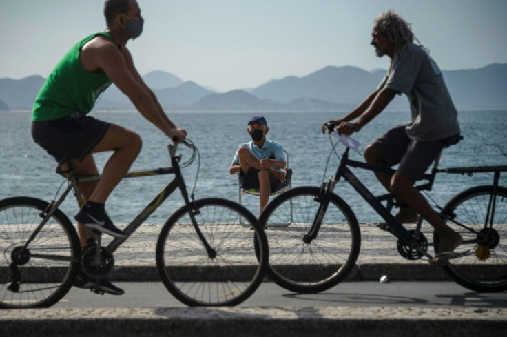 An elderly man wearing a face mask sunbathes as cyclists pass by on the promenade of Copacabana beach in Rio de Janeiro