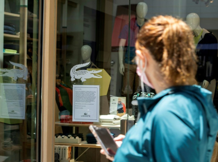 A person wearing a mask walks by a Lacoste store on Rodeo Drive in Beverly Hills where a sign says the shop will remain closed