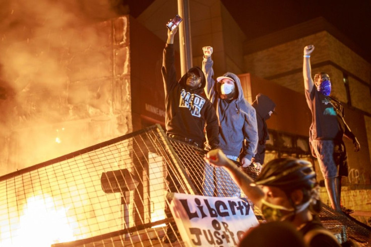 Protesters hold up their fists as flames rise behind them in Minneapolis, Minnesota, during a protest over the death of African American George Floyd in police custody