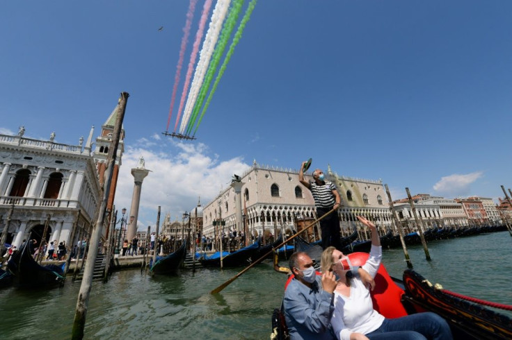 People taking a gondola ride and a gondolier wave as the Italian Air Force acrobatic unit perform over Venice
