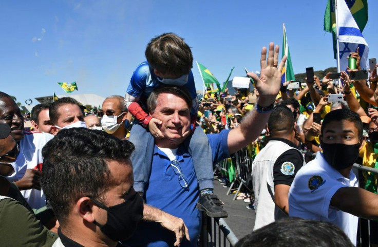 Brazilian President Jair Bolsonaro carries the son of a supporter on his shoulders as he greets supporters at a rally outside the presidential palace
