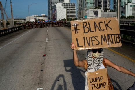 A protestor holding a Black Lives Matter / Dump Trump sign stands in front of a Florida state trooper line during a rally in Miami