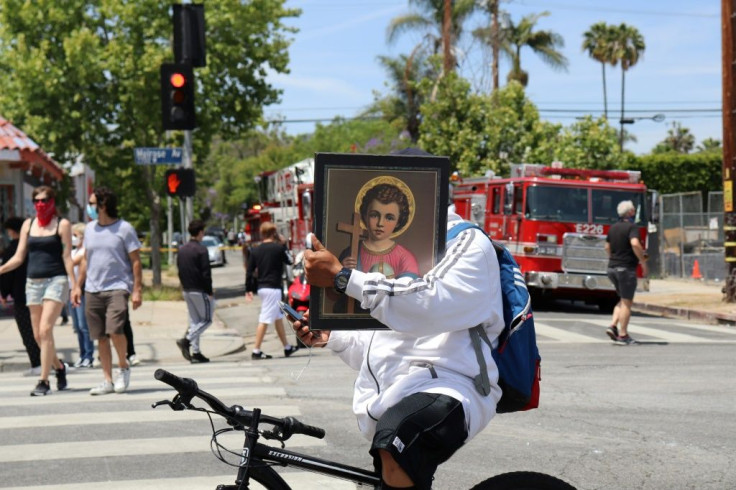 A man rides his bike carrying a religious poster as people armed with gloves and brooms get together to clean the Melrose neighborhood of Los Angeles