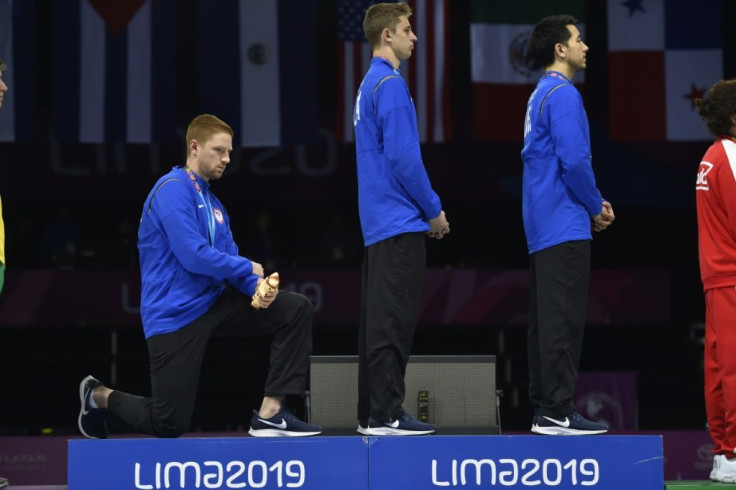 US fencer Race Imboden kneels on the medal podium at the 2019 Pan-American Games in Lima