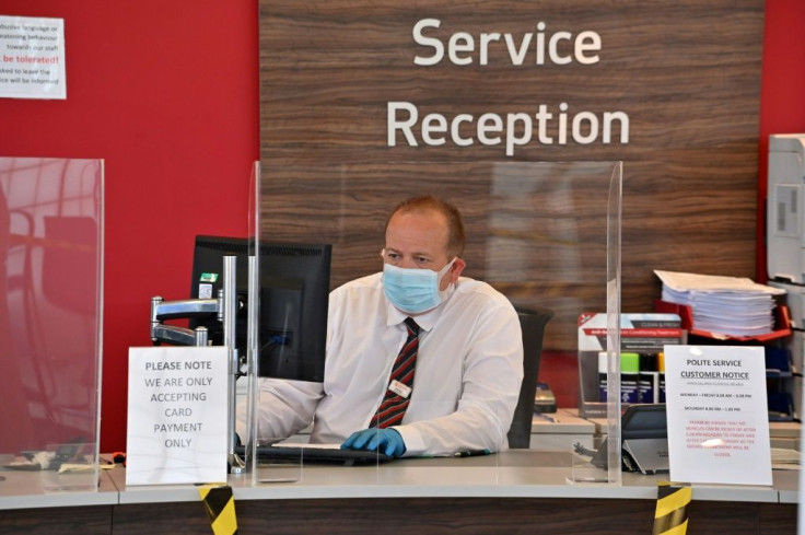 An employee dons a face mask and gloves and sits behind a perspex screen to receive customers -- many industry experts expect it will take some months for business to get back to normal