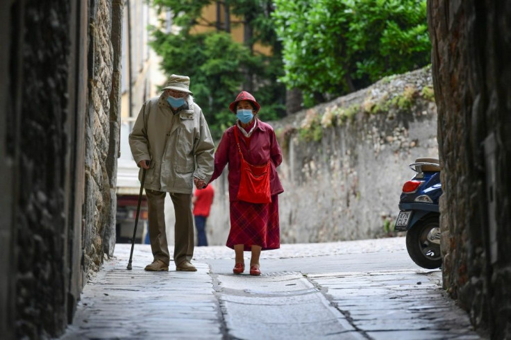 An elderly couple wearing face masks and holding hands walk in a street in the upper city of Bergamo, as Italy eases lockdown measures
