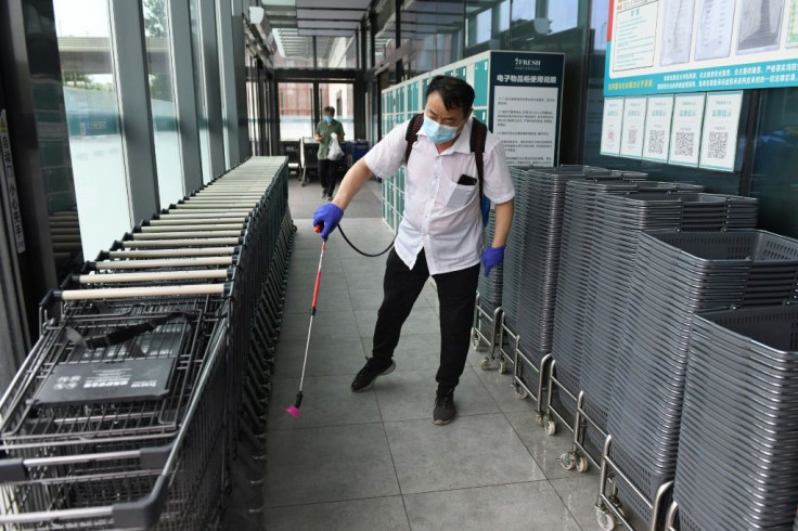 A worker disinfects shopping baskets and carts at the entrance of a supermarket in Beijing
