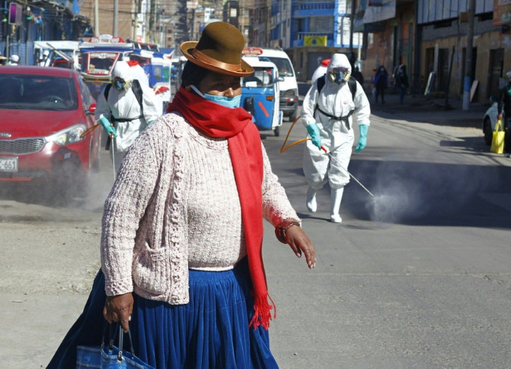 A woman dressed in typical indigenous clothing walks near municipal employees disinfecting the streets of Puno in Peru