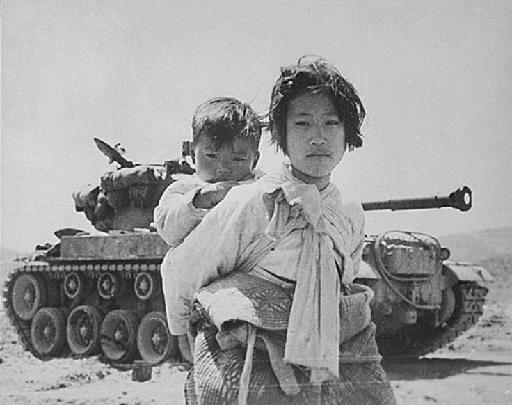 A young girl with her brother on her back walks past a stalled M-26 tank at Haengju, Korea in June 1951