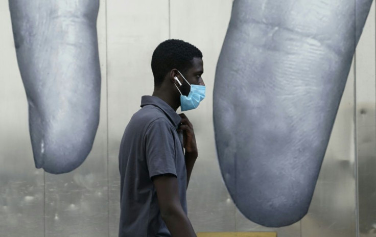 A man wearing a mask passes a mural on the side of a building in New York City