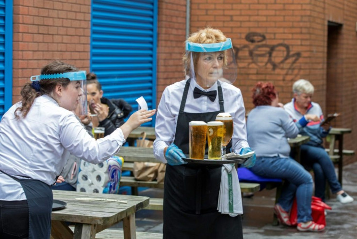 Staff wearing face shields and gloves serve people enjoying a drink in Belfast, Ireland, on July 3, 2020