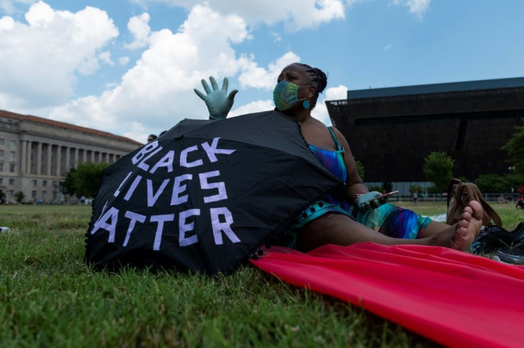 A woman sits near her umbrella during a small anti-racism rally near the Washington Monument on July 4, 2020