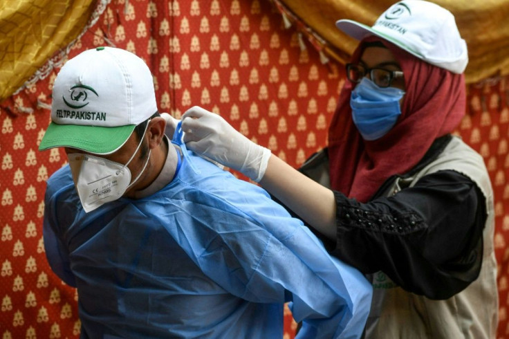 A health official helps another one to arrange protective gear before taking a test sample from patients at a drive-through screening and testing facility for the COVID-19 coronavirus in Islamabad in June 2020