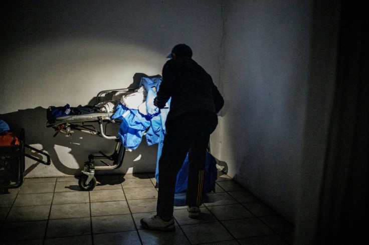 Undertaker Sello Headbush uses the light from his mobile phone during a power cut to check on a heap of discarded personal protective equipment in front of the cold storage room