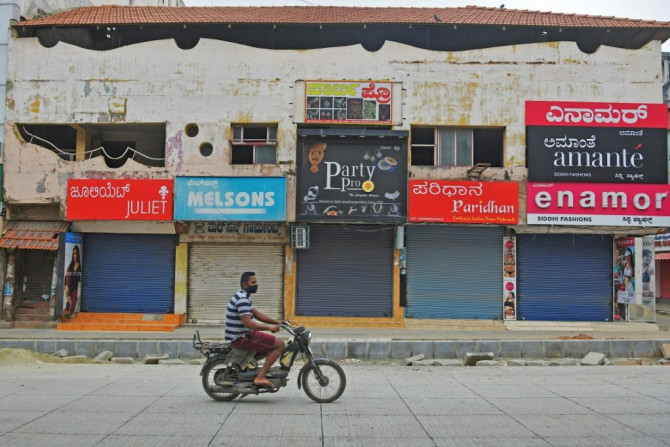 A man in a facemask rides pastshuttered shops in a commercial area  of Bangalore, India's IT hub