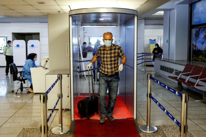 A passenger crosses with his luggage through a disinfection tunnel upon arriving on an Emirates flight in the Iranian capital Imam Khomeini International Airport
