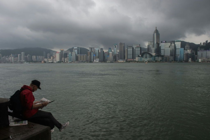 A man reads a newspaper on the edge of a promenade overlooking Victoria Harbour in Hong Kong