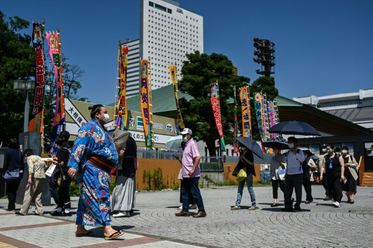 A wrestler walks past a line of people waiting to enter a two-week sumo tournament at Ryogoku Kokugikan, the main sumo arena in Tokyo