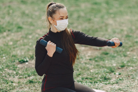sportswoman-in-face-mask-exercising-with-dumbbells-outdoors-4127320