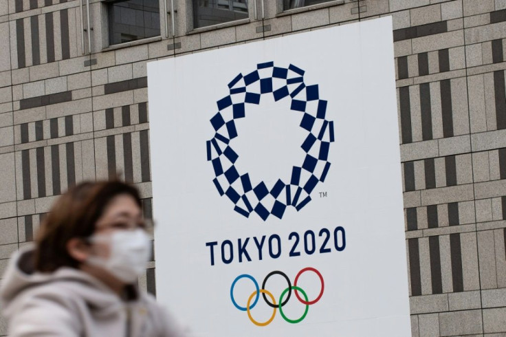A woman wearing a face mask passes in front of the 2020 Olympic Games logo outside the Tokyo Metropolitan Government Building
