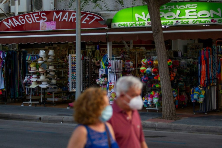 Tourists wearing face masks walk past shops in Palmanova in Mallorca