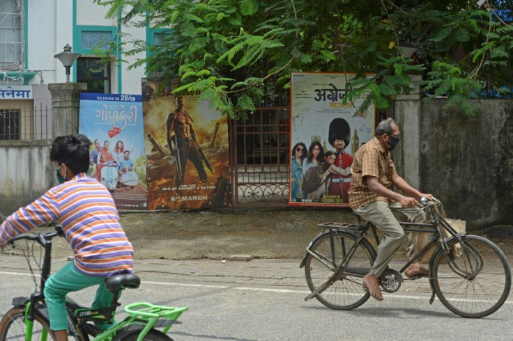 Cyclists ride past the closed gate of a Mumbai movie theatre