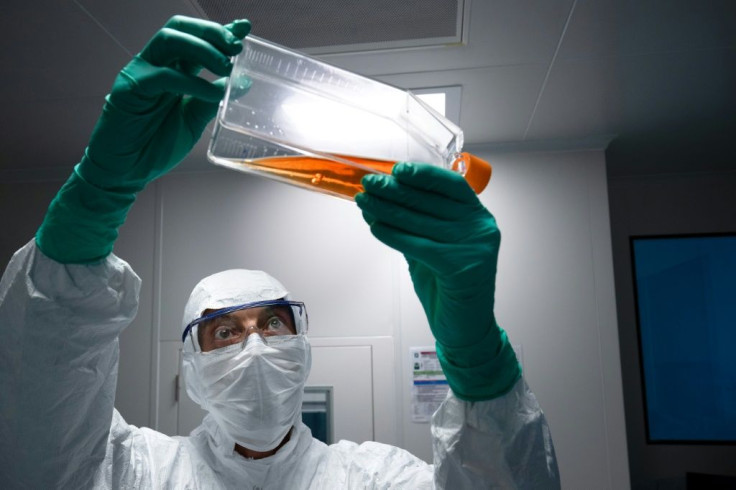A lab technician in Personal Protective Equipment (PPE) looks at a reagent bottle before performing vaccine tests at French pharmaceutical giant Sanofi's lab in Val de Reuil