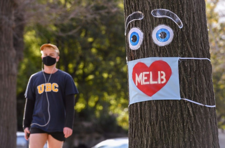 A man walks past a large face mask pinned to a tree in Melbourne after the state announced new restrictions to stop the spread of COVID-19