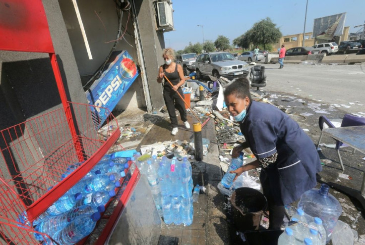 Women start to clear the damage outside a roadside kiosk in Beirut