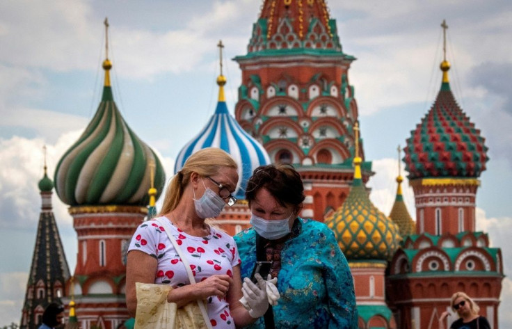 Two women wearing face masks to protect against the coronavirus stand in July 2020 in front of the Kremlin -- which the United States accuses of spreading conspiracy theories over the pandemic