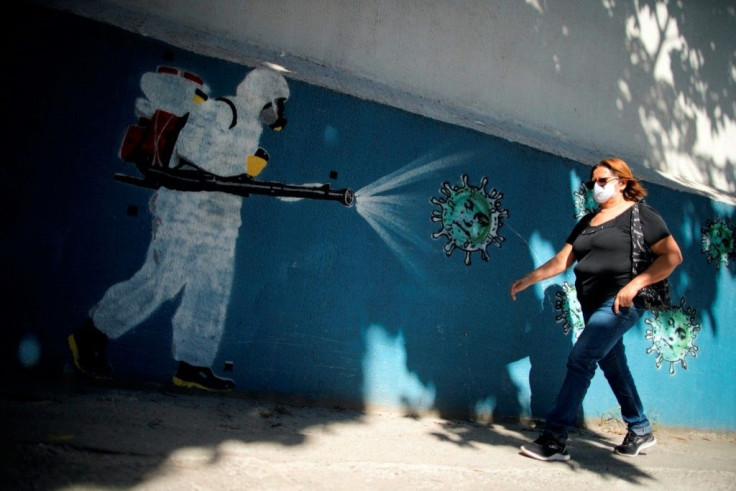 A woman walks in front of a mural depicting a man in protective suit spraying disinfectant on a coronavirus with Brazilian President Jair Bolsonaro's face, at the Tijuca neighborhood in Rio de Janeiro amid the new coronavirus pandemic in July 2020