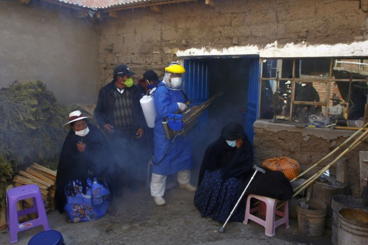 A funerary employee in protective gear disinfects the home of a COVID-19 victim as relatives mourn outside, in the remote Aymara highland village of Acora in Peru