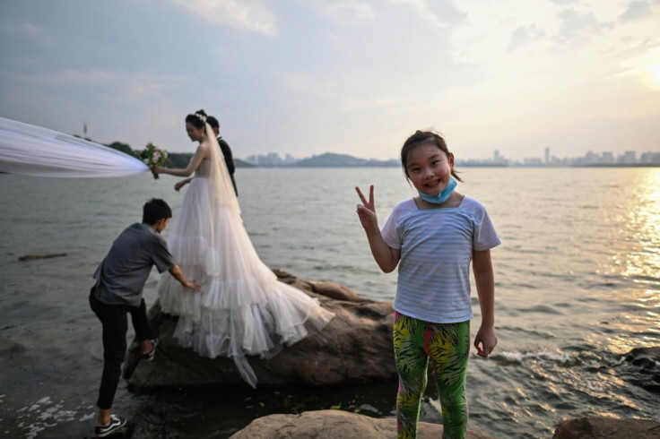 A girl gestures while a couple poses for a wedding photographer next to East Lake in Wuhan