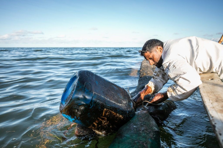 A fisherman places a hand-made oil barrier into the sea at the Old Grand Port