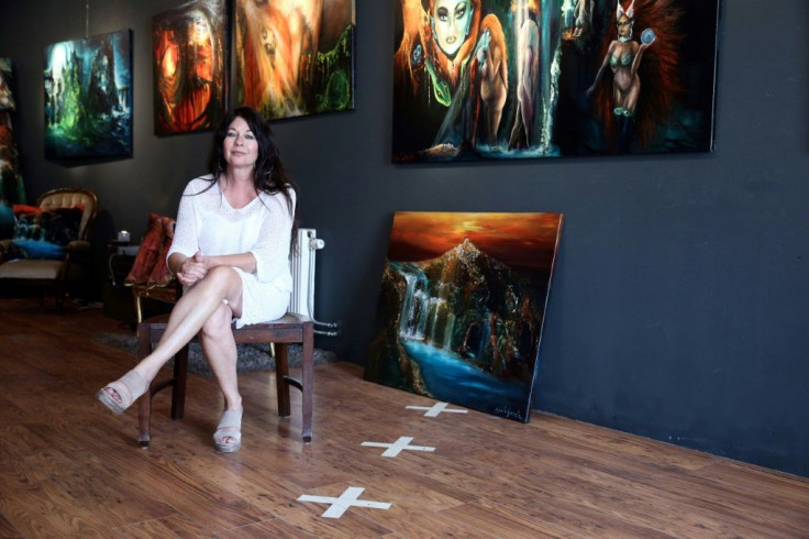 Artist Sylvia Reijbroek, who owns an art gallery that straddles the Dutch-Belgian border, sits on the Dutch side without a face mask because it is not compulsory there