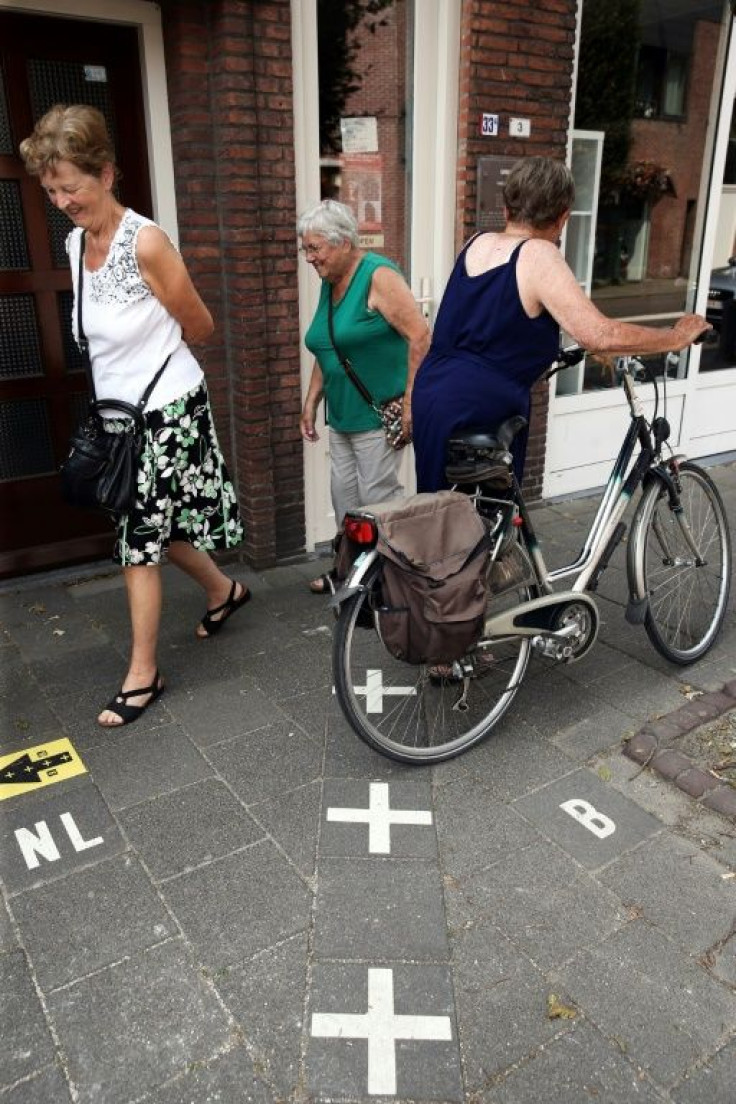 Women walk over white crosses painted on the ground separating the Netherlands and Belgium. The Belgian city of Baarle-Hertog counts 22 enclaves in Dutch territory and the Dutch city of Baarle-Nassau includes seven areas of land surrounded by Belgium