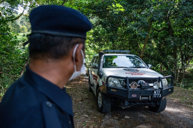 A member of the Royal Malaysia Police stands guard as a forensic vehicle leaves the main entrance of the location where Nora Quoirin's body was found