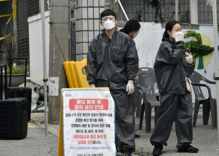 Government officials wearing protective clothing stand at a temporary check point to restrict access to the Sarang Jeil Church in Seoul