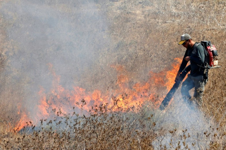 An Israeli worker from the Nature and Parks Authority tries to extinguish a fire caused by an incendiary balloon launched from the Gaza Strip, near Be'eri Kibbutz, on August 13