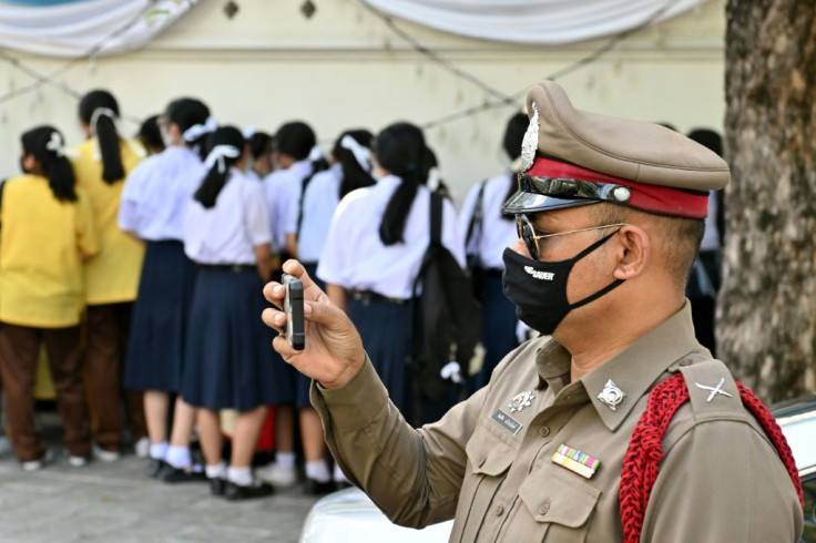 A policeman uses a mobile phone to document a protest by students in front of the Education Ministry in Bangkok