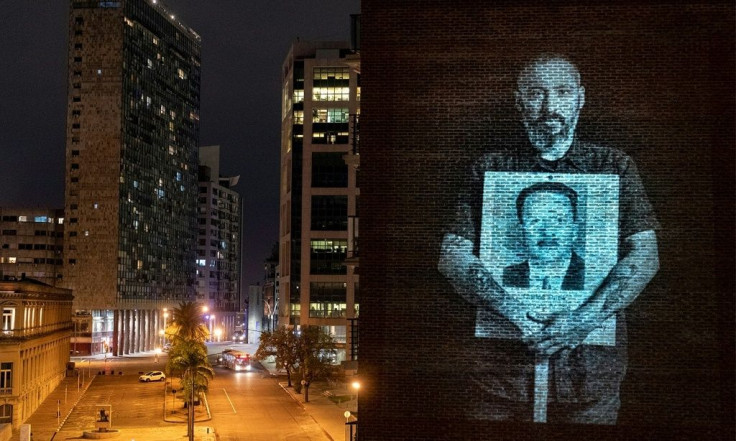 Uruguayan TV personality Diego Gonzalez holds a picture of Carlos Arevalo, who disappeared during the country's military dictatorship, in an image projected on a building in Montevideo in May 2020