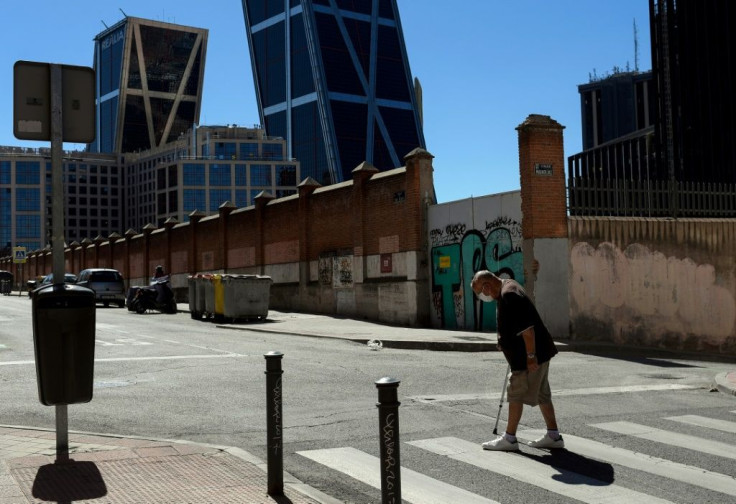 An elderly man wearing a face mask walks in Madrid with the Gate of Europe (Kio Towers) in the background