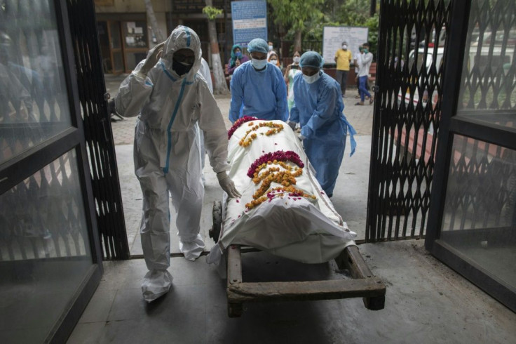 Orderlies (in blue) and a relative push a handcart carrying the body of a person who died from coronavirus to a furnace at the Nigambodh Ghat crematorium in New Delhi