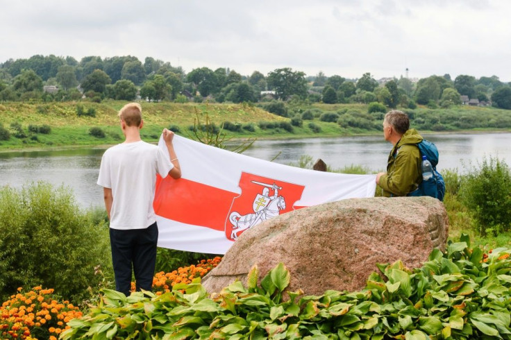 Two men hold Belarussian opposition flag near the river during a solidarity campaign for Belarussians along the border with Belarus in Piedruja, Latvia.