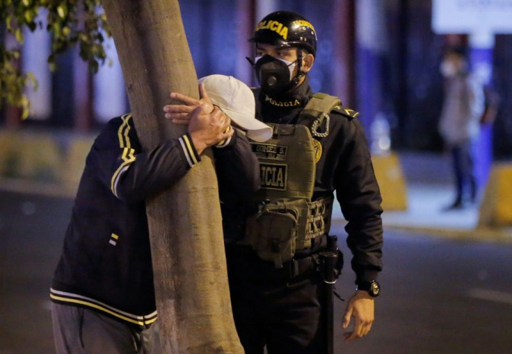 A police officer stands by as a man grieves the loss of a loved one on August 23, 2020 outside the Lima nightclub where 13 people died in a crush during a police raid