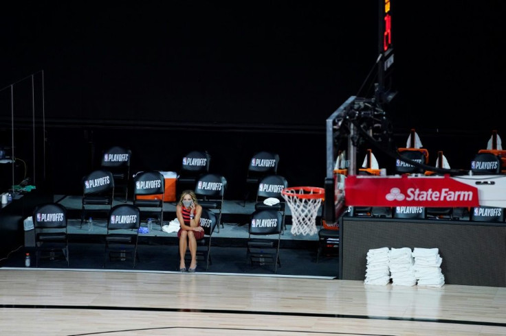 A reporter sits beside an empty court after the Milwaukee Bucks walked out of an NBA playoff game against the Orlando Magic to protest the shooting
