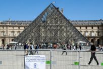 People wearing face masks walk past the Louvre Pyramid in Paris
