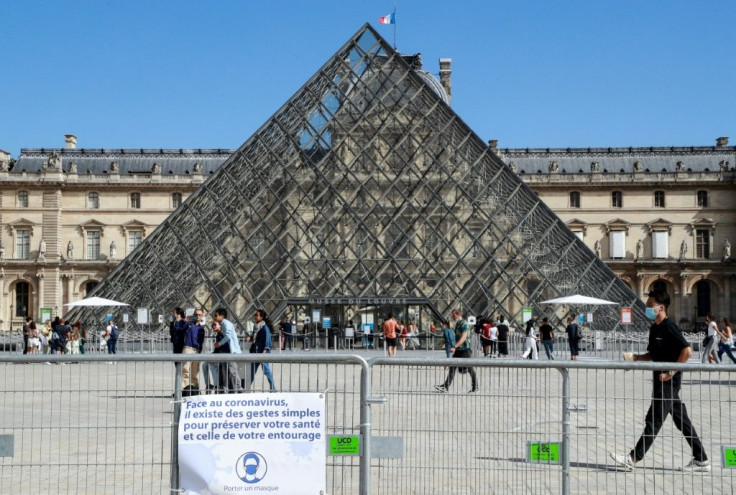 People wearing face masks walk past the Louvre Pyramid in Paris