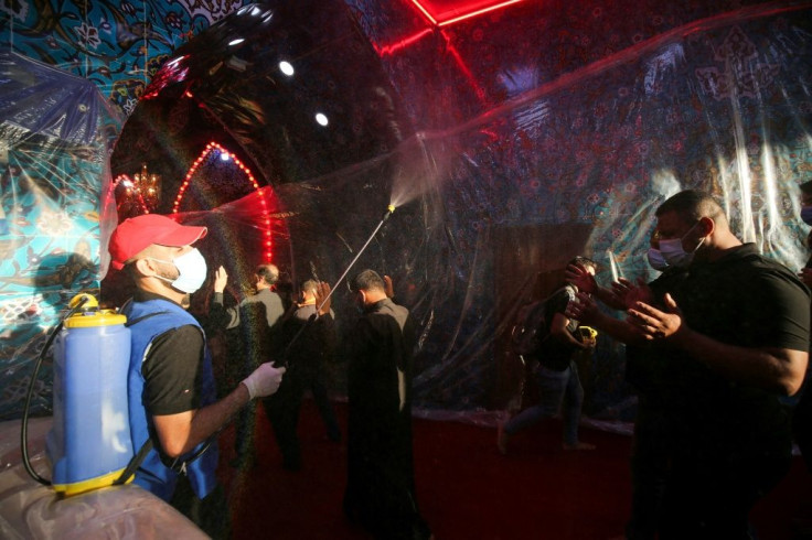 A worker sprays worshippers with disinfectant as they mourn at Imam Hussein's shrine, where the walls are covered in nylon to prevent kissing in reverence